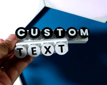 May include: Two horizontal rows of circular keys mounted on white bases. The top row features black keys with white letters spelling CUSTOM, and the bottom row features white keys with black letters spelling TEXT. Each key has a clear plastic base.