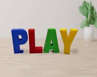 May include: Four freestanding block letters spelling the word PLAY. The letter P is blue, the letter L is red, the letter A is green, and the letter Y is yellow. Each letter is constructed with a solid, matte finish and stands upright.