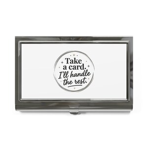 May include: A rectangular silver-toned metal business card holder with a polished finish. The centre features a white circular design with the black text "Take a card. I'll handle the rest." surrounded by small star and dot accents.