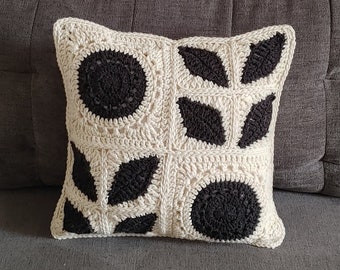 May include: A black and white crocheted throw pillow with a geometric floral design. The pillow is on a gray couch.