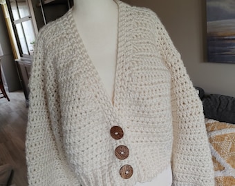 May include: A cream-colored crocheted cardigan with a V-neck and three wooden buttons.