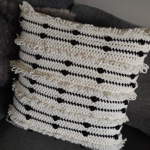 May include: A white and black crocheted throw pillow with a fringe border and black pom-poms.