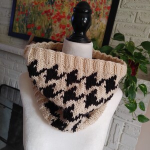 May include: A beige and black knit cowl neck scarf with a houndstooth pattern.