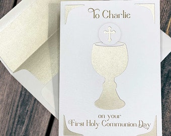 May include: White card with a gold chalice and host design. The card says "To Charlie on your First Holy Communion Day".