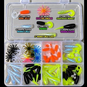 May include: A clear plastic tackle box containing various soft plastic fishing lures. The top section displays labeled samples: 2" Curly Tail Bone Jelly, 1.25" Micro Electric Chicken, 2" Curly Tail Chartreuse Monkey, 2" Crappie Slayer Monkey Milk, 2" Curly Tail Voodoo, 2" Crappie Slayer Voodoo Slayer, and 2" Monkey Milk Flash.