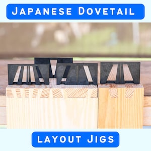 May include: Three black plastic Japanese dovetail layout jigs positioned on top of light-colored wooden boards. The jigs feature distinct geometric cutouts for marking wood joints. The text "JAPANESE DOVETAIL" and "LAYOUT JIGS" is visible.