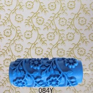 Puede incluir: Rodillo de pintura azul con un diseño floral. El rodillo mide 18 cm de largo y tiene un diámetro de 10 cm. El diseño presenta un patrón repetitivo de flores y hojas.