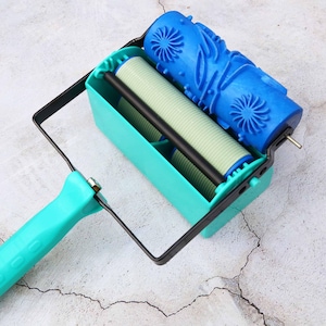 May include: A teal and black paint roller with a blue patterned roller head. The roller is designed for creating decorative patterns on walls and other surfaces.