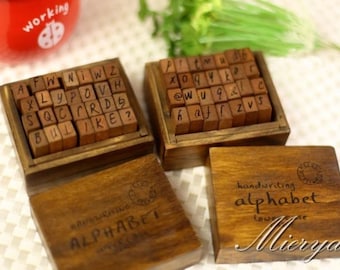 Puede incluir: Tres cajas de madera que contienen juegos de sellos de alfabeto. Cada caja tiene una etiqueta que dice "alfabeto de escritura a mano" y el nombre de la empresa "Mierya".