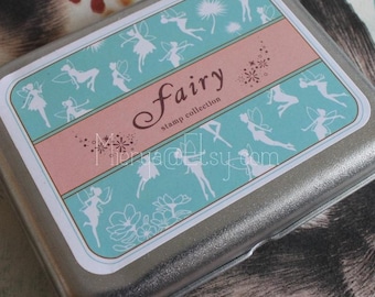 May include: A silver metal box with a teal and pink label. The label has a design of fairies and the text "Fairy stamp collection".