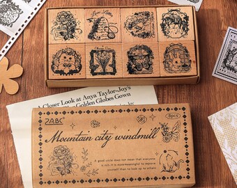 May include: A set of eight wooden stamps featuring various designs, including flowers, birds, and a windmill. The stamps are arranged in a wooden box with a label that reads "Mountain city windmill".