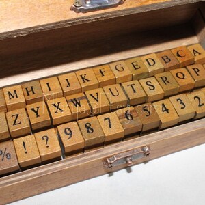 May include: A wooden box filled with alphabet and number stamps. The stamps are made of wood and have black lettering. The box is open and the stamps are visible.