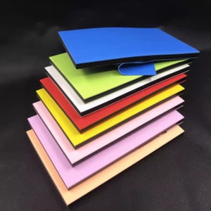 Puede incluir: Una pila de paneles rectangulares coloridos en varios tonos, incluyendo azul, verde, rojo, amarillo y rosa. Cada panel tiene un borde negro y un interior blanco o negro, creando un efecto de capas. Los paneles están dispuestos en ángulo, mostrando sus colores vibrantes.