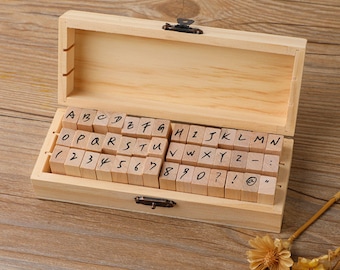 May include: Wooden box containing a set of alphabet and number stamps. The stamps are made of wood and have black ink. The box is open and the stamps are visible. The stamps are arranged in alphabetical and numerical order.
