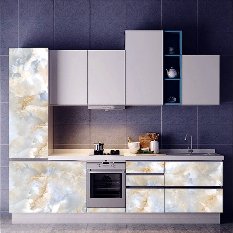 May include: White kitchen cabinets with marble-patterned doors. The cabinets are arranged in a row with a built-in oven and a countertop with a sink and stove.