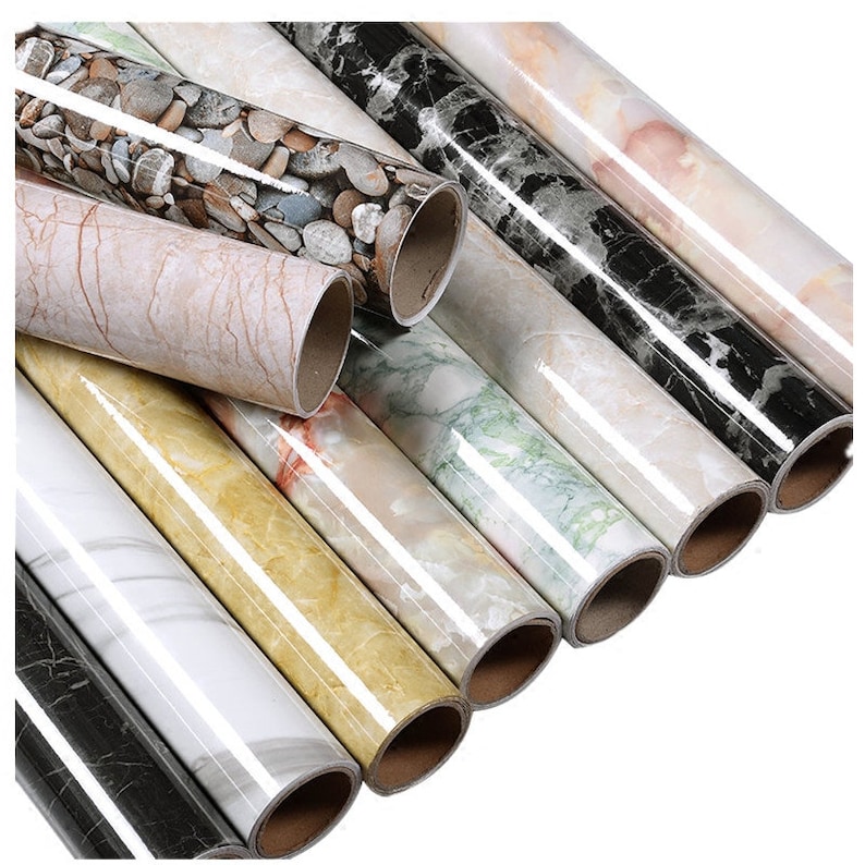 May include: Rolls of self-adhesive vinyl contact paper with marble and stone patterns. The rolls are in various colors, including white, black, brown, and green.