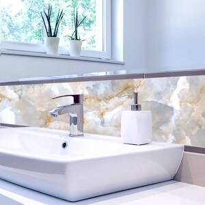 May include: A white porcelain bathroom sink with a chrome faucet and a white soap dispenser. The sink is set against a backdrop of white and gold marble tile.