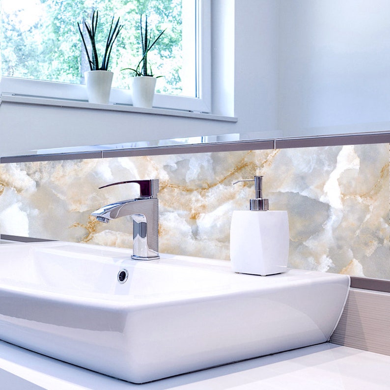 May include: A white porcelain bathroom sink with a chrome faucet and a white soap dispenser. The sink is set against a backdrop of white and gold marble tile.