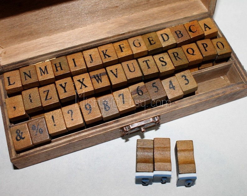 May include: A wooden box filled with letter and number stamps. The stamps are made of wood and have black lettering. The box is open and the stamps are visible. There are three additional stamps outside of the box.