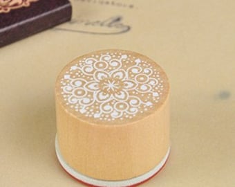 May include: A round wooden stamp with a white intricate design of a mandala. The stamp has a red rubber base.