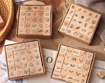 May include: Four boxes of wooden stamps with different designs. One box has weather symbols, another has leaves and flowers, a third displays butterflies, and the last shows facial expressions. The stamps are small, square blocks.