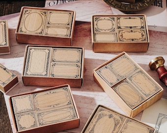 May include: A collection of wooden stamps with decorative frames and blank spaces, presented in small cardboard boxes. The stamps feature various shapes, including rectangles and ovals, with detailed border designs. The color scheme is natural wood tones with black ink details.