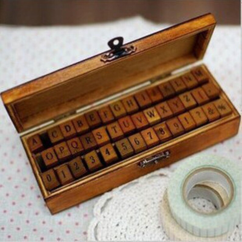 May include: A wooden box with a latch contains a set of alphabet and number stamps. The stamps are made of wood and have black lettering. The box is open and the stamps are visible.