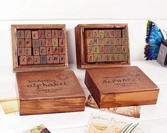 Puede incluir: Dos cajas de madera con sellos de alfabeto. Las cajas son marrones y tienen una etiqueta que dice "alfabeto de escritura a mano" y "minúsculas" en una caja y "alfabeto de escritura a mano" y "mayúsculas" en la otra caja.