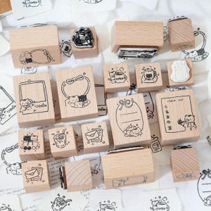 May include: A collection of wooden stamps featuring various designs, including a coffee cup, a check list, a frame, a gift box, and a bear holding a cup of coffee. The stamps are all made of natural wood and have a light brown color.