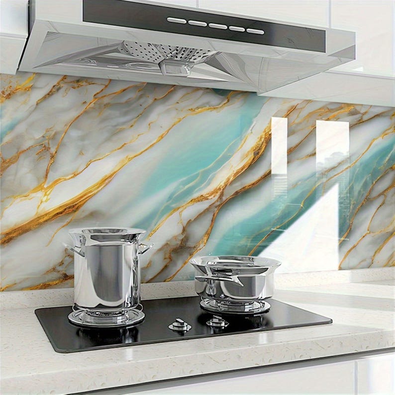 Peut inclure: Une cuisini&egrave;re &eacute;lectrique noire avec deux casseroles argent&eacute;es dessus. La cuisini&egrave;re est devant un dosseret de cuisine avec un motif de marbre dans des tons de bleu, blanc et or.