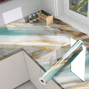 Peut inclure: Un rouleau de papier contact marbr&eacute; bleu et or avec un dos blanc. Le papier contact est d&eacute;roul&eacute; sur un plan de travail avec un motif marbr&eacute;.