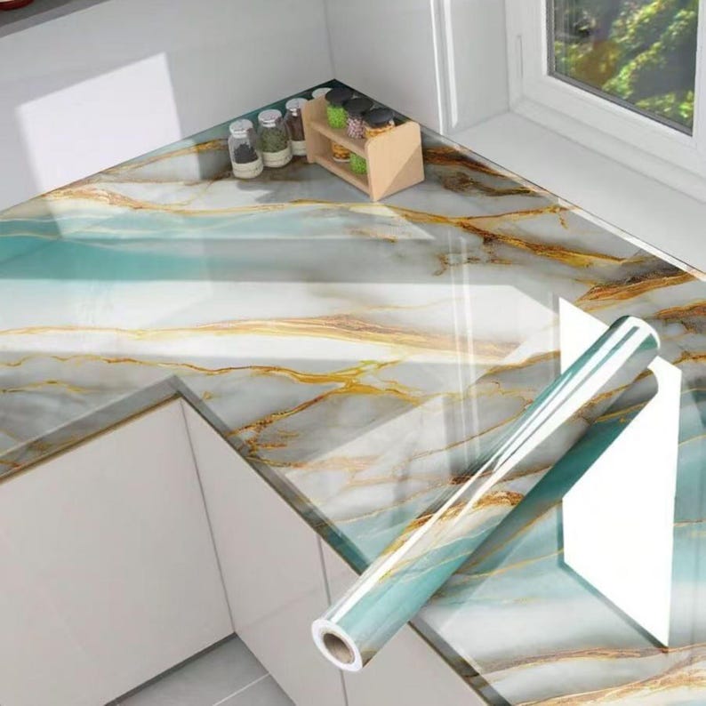 Peut inclure: Un rouleau de papier contact marbr&eacute; bleu et or avec un dos blanc. Le papier contact est d&eacute;roul&eacute; sur un plan de travail avec un motif marbr&eacute;.