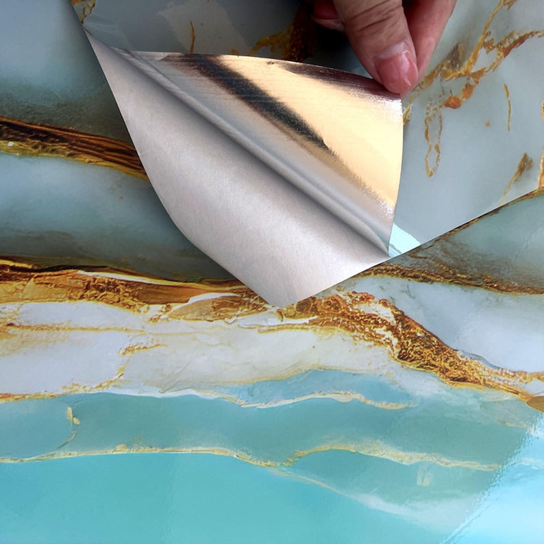 Peut inclure: Gros plan sur un papier contact marbr&eacute; turquoise et or avec un dos argent&eacute;. Le dos est d&eacute;coll&eacute; pour r&eacute;v&eacute;ler le c&ocirc;t&eacute; adh&eacute;sif du papier.