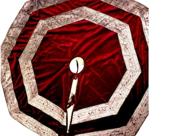 May include: A circular deep red velvet tree skirt featuring two concentric octagonal borders with intricate silver and white floral embroidery. The fabric has a central circular cutout and a slit opening with matching fabric ties.