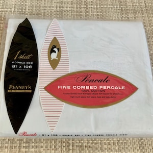 May include: A packaged white double bed sheet. The packaging includes a black oval with "1 sheet" and "206 x 274 cm" in white text. A red and gold oval label reads "Fine Combed Percale".