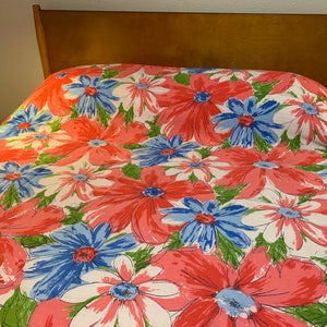 May include: A white bedspread with a large-scale floral print featuring pink, blue, and green flowers. The bedspread is on a wooden bed frame.