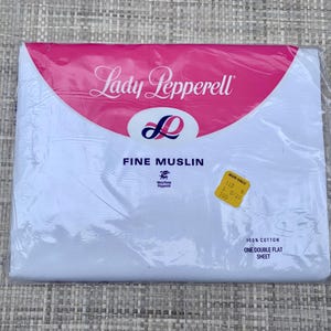 May include: A packaged white flat sheet with the text "Lady Pepperell" in a pink and white design. The package also includes the text "FINE MUSLIN" and a yellow price tag. The sheet is made of 100% cotton.