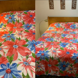 Op de afbeelding: Een wit bedovertrek met een grootschalige bloemenprint met roze, blauwe en groene bloemen. Het bedovertrek ligt op een houten bedframe.