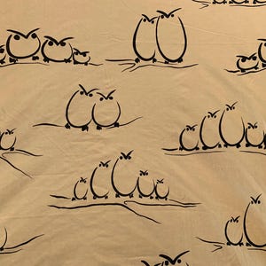 May include: Tan fabric with a repeating pattern of black owl illustrations. The owls are depicted in various groupings, from pairs to families, perched on thin, curved branches. The design has a simple, sketched aesthetic.