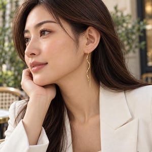 May include: A gold threader earring featuring a delicate, wavy, serpentine metal wire that hangs vertically from the earlobe, complemented by a thin, straight chain segment that extends downward, creating a sleek and elongated silhouette.