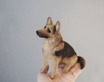 May include: A brown and black needle felted German Shepherd dog figurine. The dog is sitting with its head turned to the side and its tail curled.
