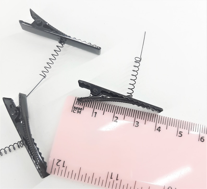 May include: Three black metal hair clips with spring coils. The clips are approximately 4 cm long and are shown next to a ruler.