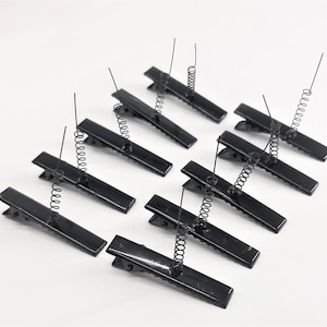 May include: Ten black metal hair clips with a spring on the top. The clips are all in a row, with the springs facing up.