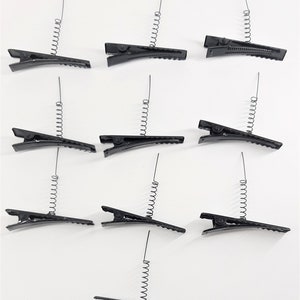 May include: Twelve black spring-loaded hair clips. Each clip has a metal spring that extends from the top of the clip.