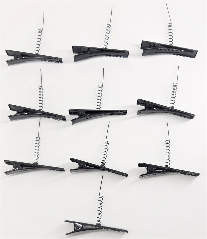 May include: Twelve black spring-loaded hair clips. Each clip has a metal spring that extends from the top of the clip.