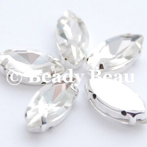 May include: Five clear, marquise-shaped rhinestones with silver-colored metal settings. The rhinestones are faceted, reflecting light. The image includes the text "Beady Beau".