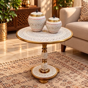 May include: A round side table with a gold metal frame and a white tabletop featuring intricate black and red patterns. Two matching lidded jars with similar white, black, and red decorative motifs sit on the table surface. The table has a central pedestal base with a circular foot, all decorated with detailed patterns.