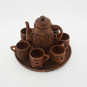 Peut inclure: Un service à thé en bois brun foncé composé d'une théière centrale avec couvercle, de six petites tasses avec anses et d'un plateau de service circulaire. La théière et les tasses présentent des sculptures florales et des motifs texturés.