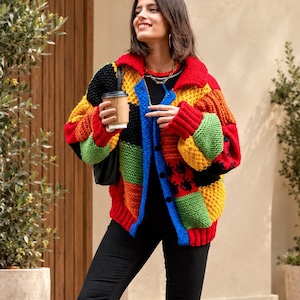 May include: A chunky knit cardigan featuring a vibrant patchwork design with blocks of red, yellow, green, black, and orange yarn. The garment has a collared neckline, long sleeves with ribbed cuffs, and a front button closure. The logo ElvaneWear is visible.