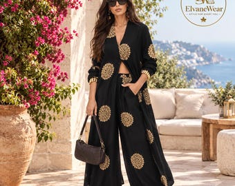 May include: A black two-piece set consisting of a long-sleeved duster cardigan and wide-leg trousers, both featuring a repeating gold circular mandala-style pattern. The outfit is paired with a dark brown handbag and black sunglasses.